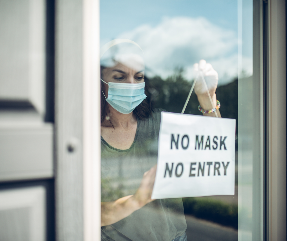 Image of a store own putting up a sign that says "no mask, no entry"